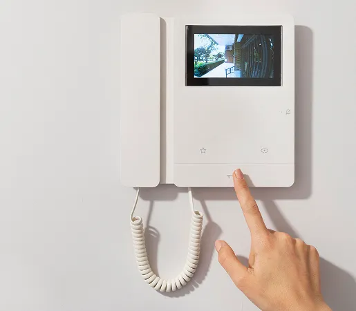 Main décrochant le combiné d’un portier visiophone à écran fixé au mur